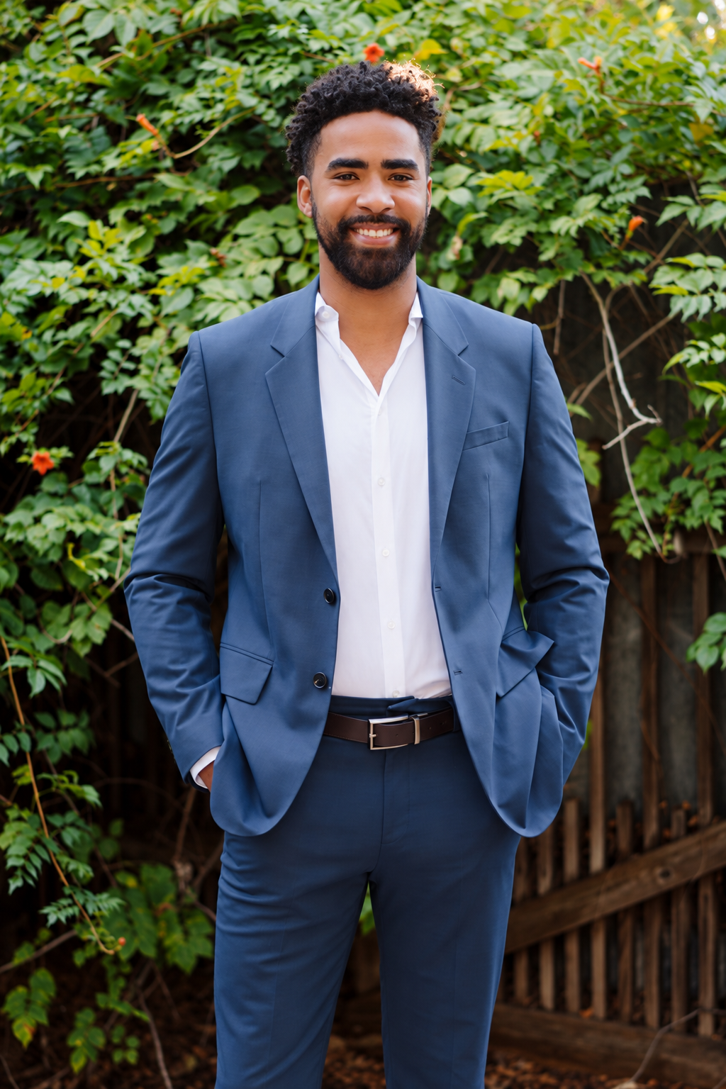 Brandon Taylor smiling in a blue suit in front of garden greenery