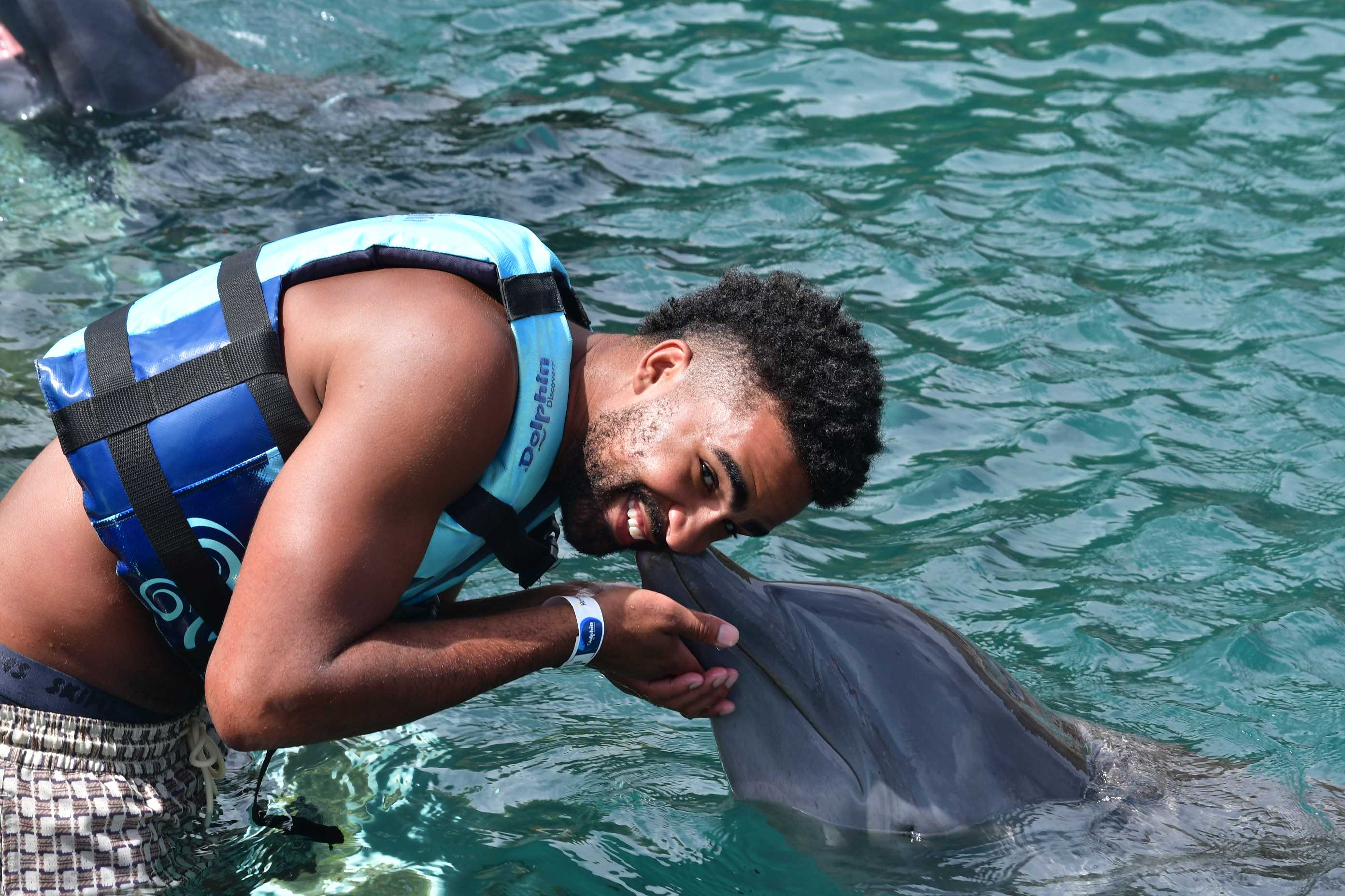 Smiling man in a blue life jacket leaning toward a dolphin