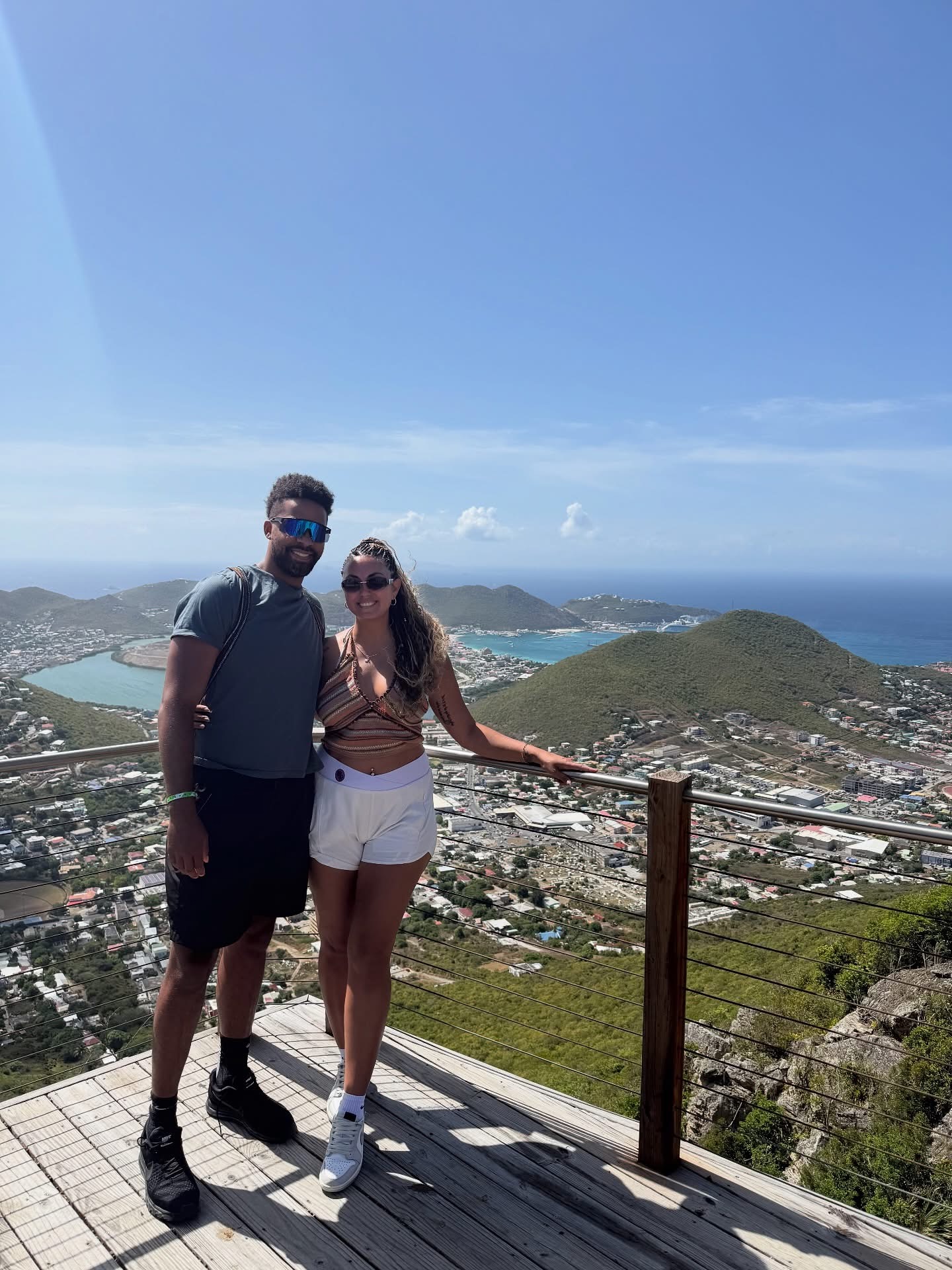 Two travelers at a mountain overlook above a coastal town