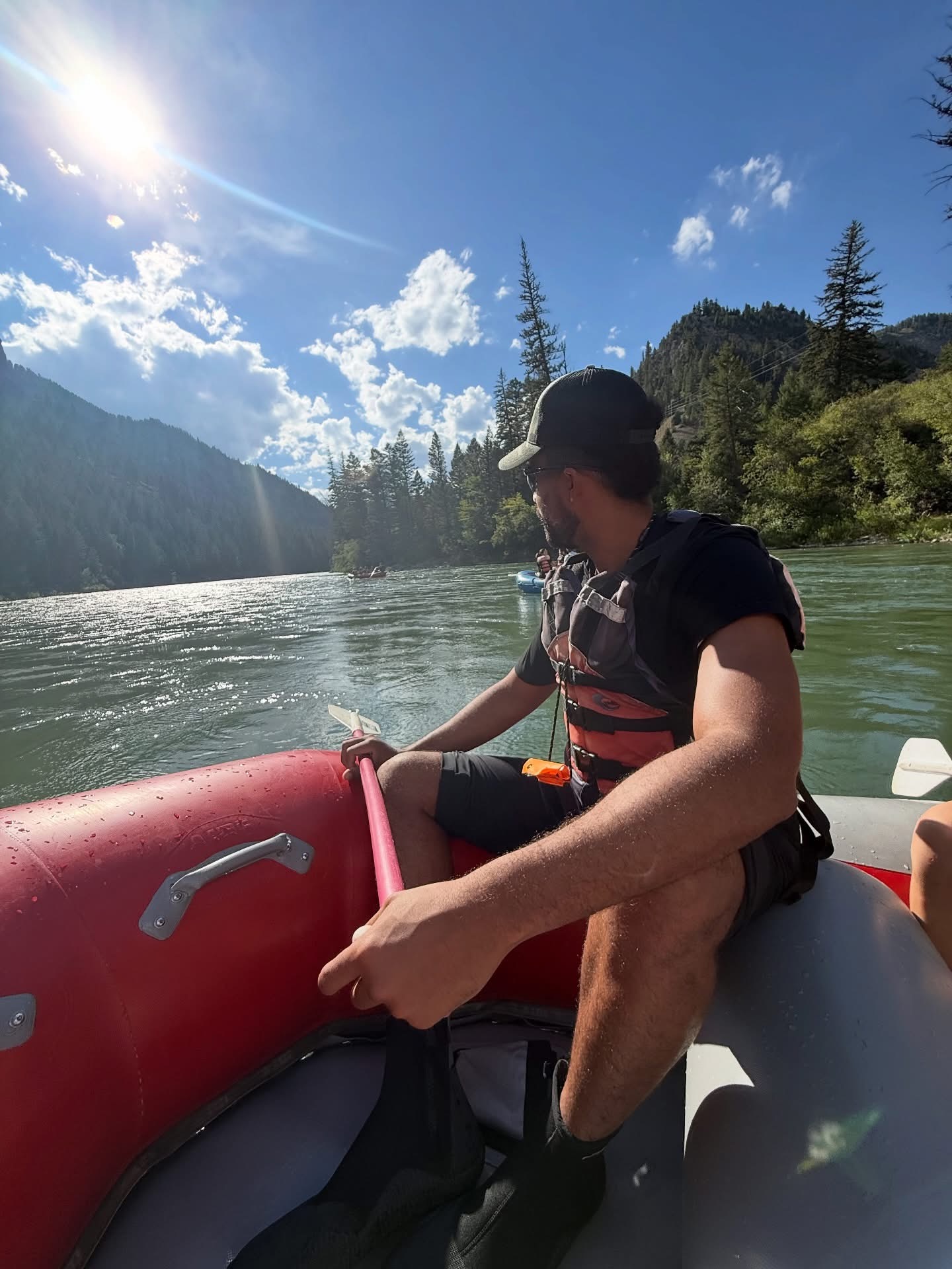 Rafter holding a paddle on a river surrounded by forested mountains