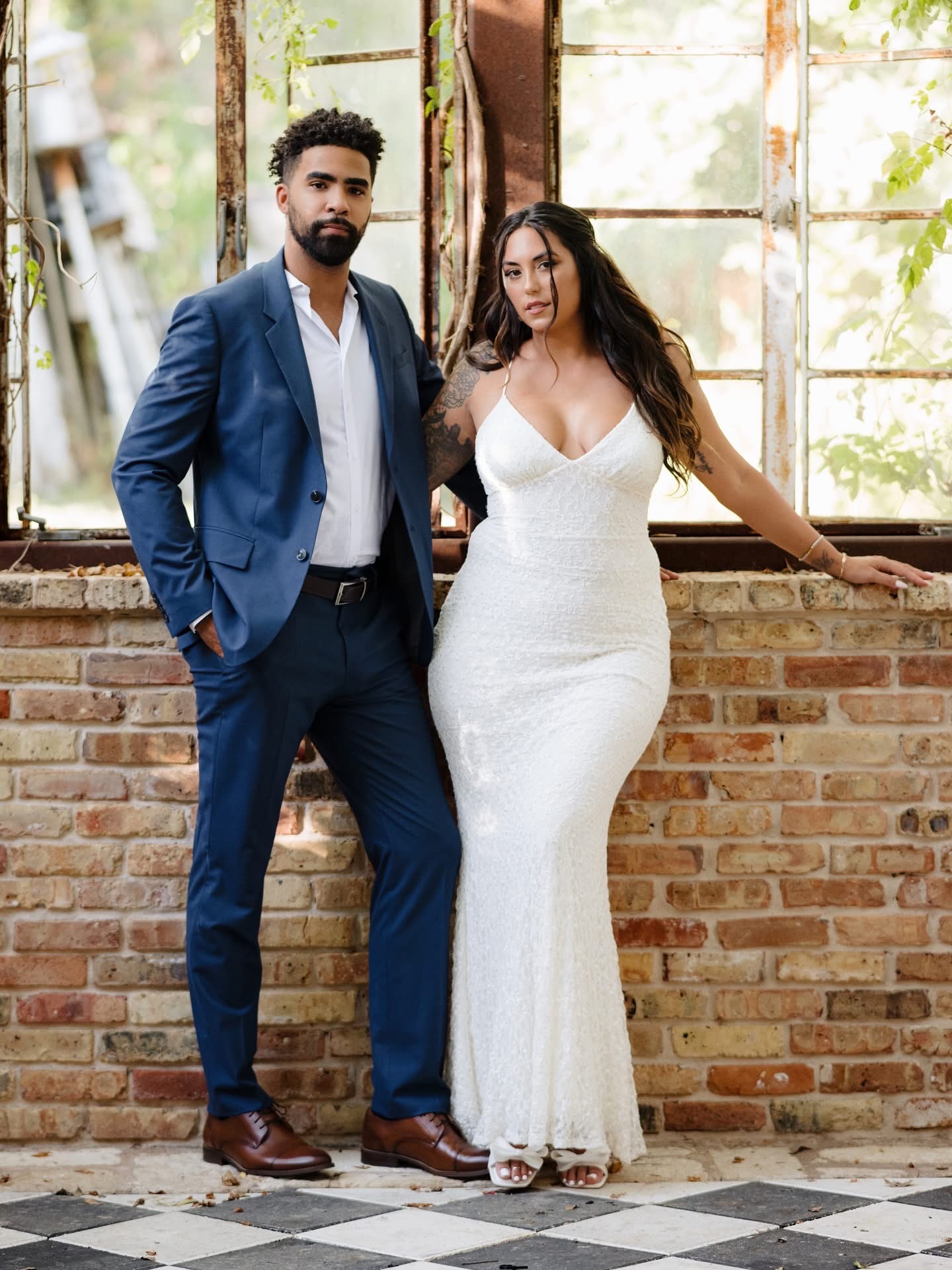 Couple posing in formal attire beside tall windows