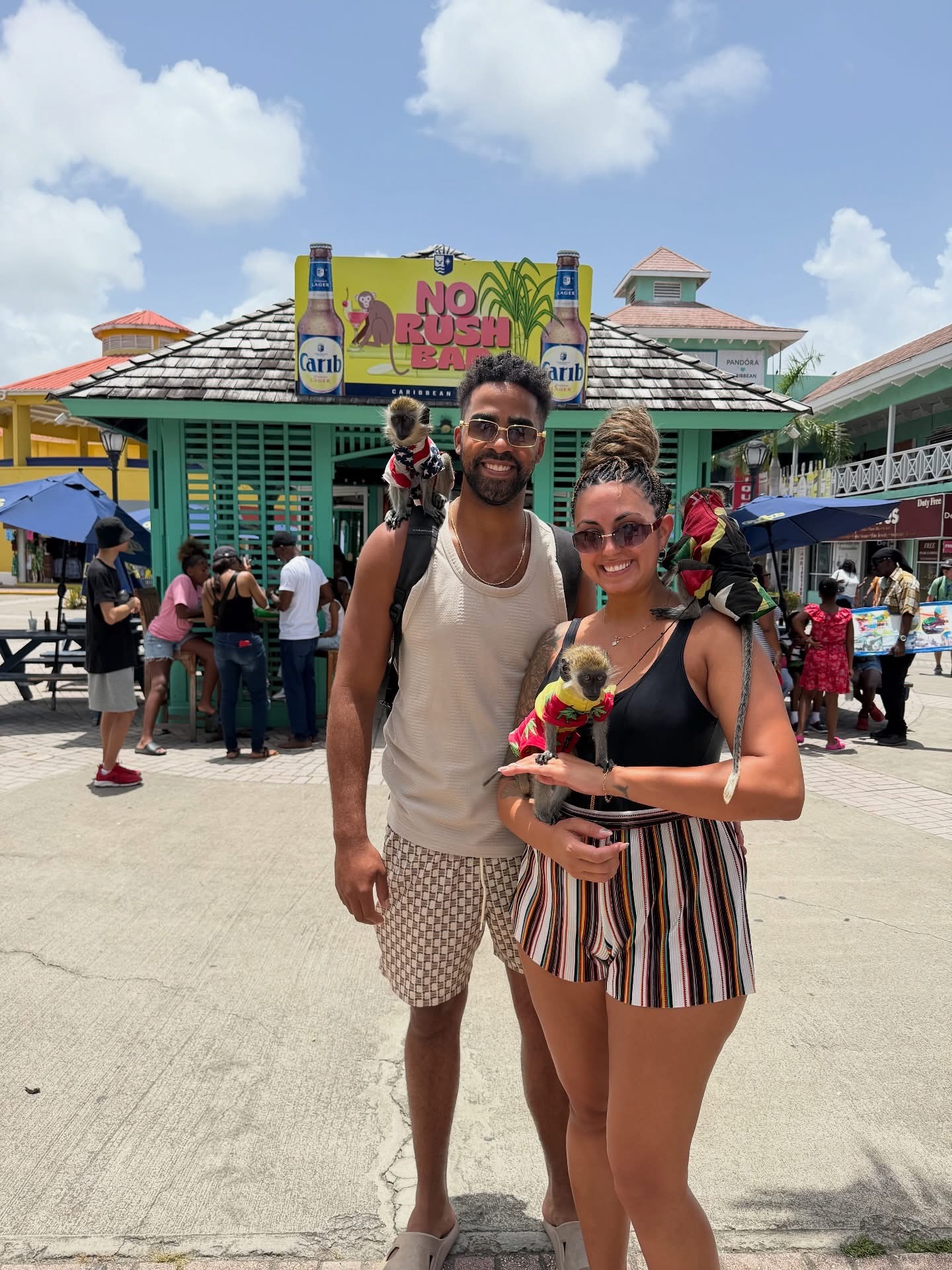 Two travelers posing with small monkeys in a sunny plaza